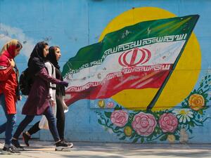 Young girls walk in front of a mural showing the Iranian national flag (AFP)
