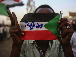 Sudanese protester holds the national flag with writings reading in Arabic "Civilian Only"  (AFP)