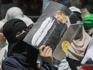 A woman wearing a niqab (full face veil) holds up a sign showing Egypt's late ousted president Mohamed Morsi, with captions in Arabic reading "our souls all long for Jerusalem, the martyr Mohamed Morsi" (AFP)