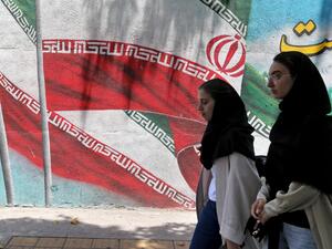 Iranian women walk past a mural painted with the Iranian flag in Tehran (AFP)