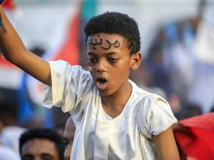 A Sudanese boy wearing facepaint on his forehead reading in Arabic "civilian" chants slogans while seated on the shoulders of a man as people celebrate after protest leaders struck a deal with the ruling generals on a new governing body, in the capital Khartoum's eastern district of Burri (AFP)