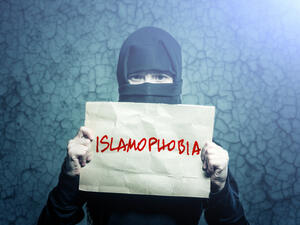 Muslim girl in black hijab holding a poster with an inscription ISLAMOPHOBIA (Shutterstock)