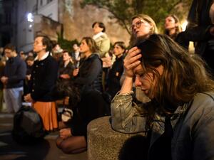 People kneel on the pavement as they pray outside watching flames engulf Notre-Dame Cathedral in Paris on April 15, 2019. A colossal fire swept through the famed Notre-Dame Cathedral in central Paris on April 15, 2019. (AFP)