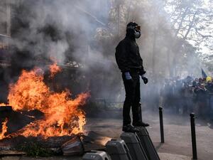 A masked protester dressed in black stands next to a burning barricade during clashes on the sidelines of a May Day demonstration in Paris, on May 1, 2019. (Anne-Christine POUJOULAT / AFP)
