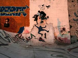 Palestinian youths play with rollerblades by walls covered with graffiti at the sea port in Gaza City on 19 June, 2018. [MAHMUD HAMS/AFP]
