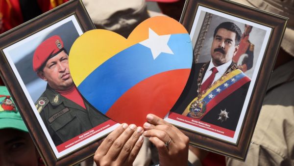 A supporter of Venezuelan President Nicolas Maduro displays pictures of Maduro (R) and late leader Hugo Chavez during a rally on May Day in Caracas on May 1, 2019. (AFP/ File Photo)