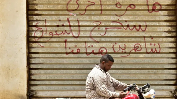 A Sudanese man sits on a motorbike in front of a closed photo studio in Khartoum on June 9, 2019. Arabic writing on the shutters of the closed shop reads: "Another time, we shall take to the streets, crying out our demands loudly." (AFP/ File Photo)