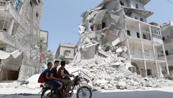 A Syrian man drives a motorcycle past destroyed buildings in the town of Ariha, in the south of Syria's Idlib province (AFP)