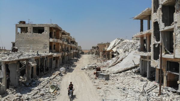 Syrian men riding a motorcycle past the rubble of destroyed buildings in the town of Khan Sheikhun in the southern countryside of Idlib. (AFP/ File Photo)