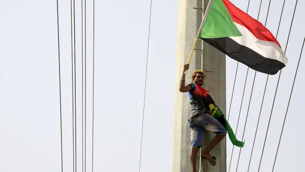 A Sudanese demonstrater waves his national flag in front of the Algerian embassy as people celebrate in Khartoum (AFP)