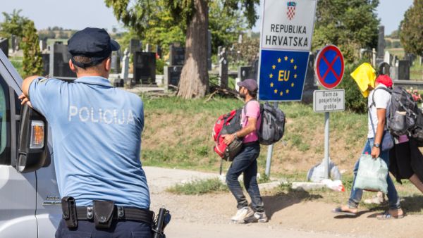 Croatian police officer looking at Refugees passing in front of the EU entrance sign on the Serbia-Croatia border crossing. (Shutterstock/ File Photo)