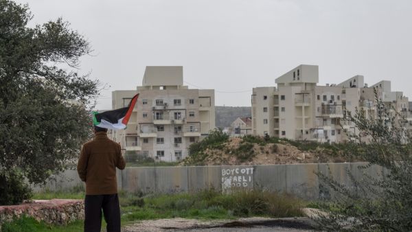 A Palestinian protester stands near the West Bank Barrier holding a flag as a form of protest in Bilin, West Bank, Palestine. (Shutterstock/ File Photo)