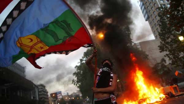A demonstrator flutters a Mapuche indigenous flag near a bonfire in Santiago, on October 25, 2019, a week after violent protests started. Demonstrations against a hike in metro ticket prices in Chile's capital exploded into violence on October 18, unleashing widening protests over living costs and social inequality. (Pablo VERA / AFP)