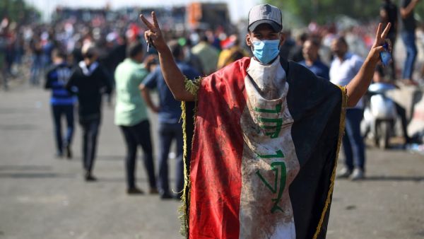 An Iraqi protester, draped in a national flag, flashes the victory sign near the capital Baghdad's Al-Jumhuriyah Bridge on October 26, 2019, during an anti-government rally. Iraqi security forces fired tear gas to clear lingering protesters in Baghdad this morning, after dozens died in a bloody resumption of anti-government rallies to be discussed in parliament. (AFP)