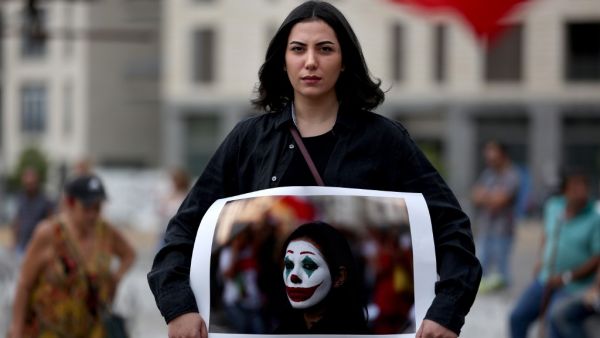 Lebanese protester Cynthia Aboujaoude holds a picture of her face painted as the Joker in downtown Beirut on October 23, 2019 as demonstrations to demand better living conditions and the ouster of a cast of politicians who have monopolised power and influence for decades continue. Patrick BAZ / AFP