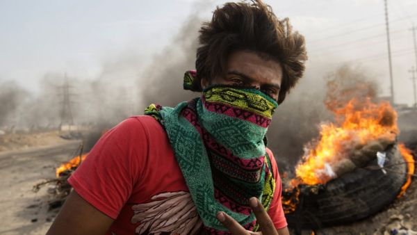 An Iraqi protester walks past burning tires as others block the road to Umm Qasr port during ongoing anti-government demonstrations in southern Iraq on November 7, 2019. A sit-in had cut the road to the Umm Qasr port, which brings in most food and medical imports through Basra, but it reopened later during the day. Hussein FALEH / AFP