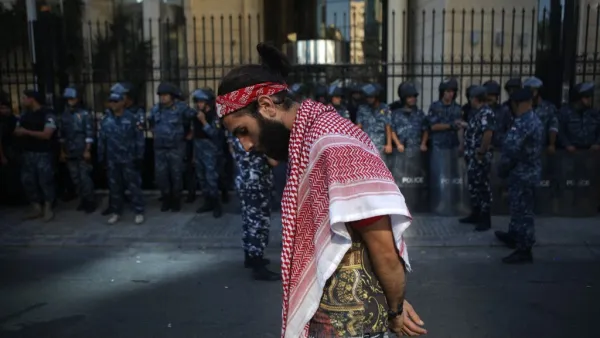 A Lebanese protester draped in a traditional Palestinian Keffiyeh scarf walks past a row of security forces during ongoing anti-government demonstrations in central Beirut  (AFP)
