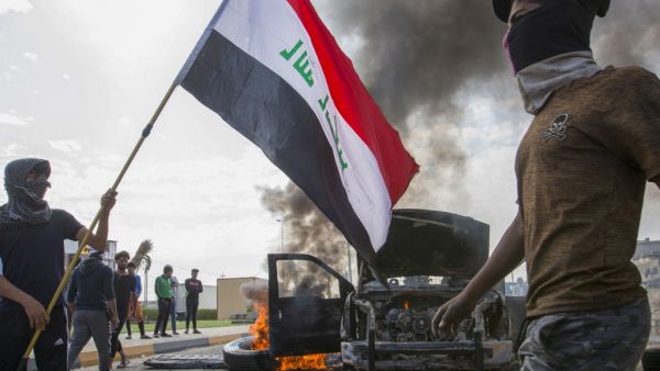 Iraqi demonstrators stand next to the smoking remains of an Iraqi anti-riot vehicle during a demonstration in the southern city of Basra on November 24, 2019, as protesters cut-off roads and activists call for a general strike.  (AFP/ File Photo)
