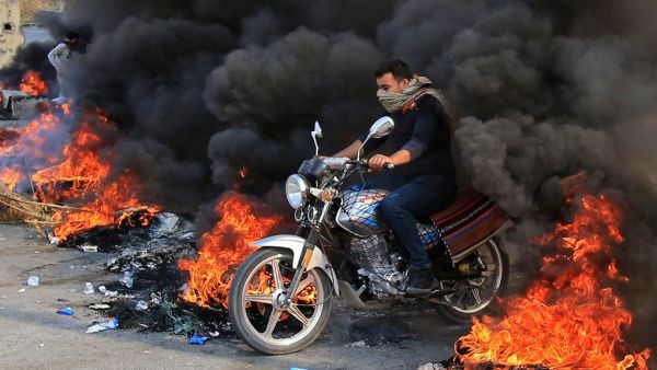 An Iraqi man drives through burning tires in the Shiite Muslim shrine city of Karbala, south of Iraq's capital Baghdad, on November 26, 2019. Since October 1, Iraq's capital and majority-Shiite south have been swept by mass rallies against corruption, a lack of jobs and poor services that have escalated into calls for a complete overhaul of the ruling elite. Mohammed SAWAF / AFP