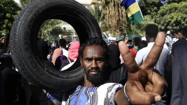Sudanese protester flashes the victory gesture while holding a car tire on his shoulder during a demonstration in the centre of Sudan's capital Khartoum outside the prime minister's offices (AFP)