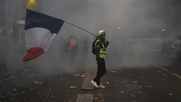A man holding a French flag and a yellow vest walks in tear gas during a demonstration against the pension overhauls, in Paris, on December 5, 2019 as part of a nationwide strike. Trains cancelled, schools closed: France scrambled to make contingency plans on for a huge strike against pension overhauls that poses one of the biggest challenges yet to French President's sweeping reform drive. Zakaria ABDELKAFI / AFP