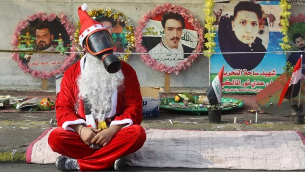 An Iraqi demonstrator wearing a Santa Claus costume and a gas mask sits on a blanket in the capital Baghdad's Tahrir Square, amid ongoing anti-government protests, on December 6, 2019.  (AFP/ File Photo)
