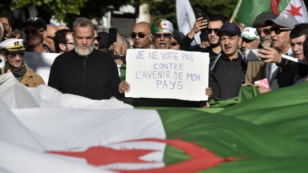 Algerian protesters march with national flags and signs, one in French reading "I will not vote against the future of my country", during a demonstration against the upcoming presidential election, in the capital Algiers on December 10, 2019. RYAD KRAMDI / AFP