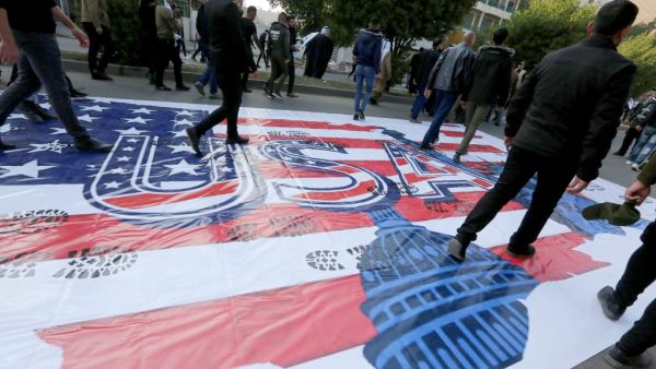 Supporters of Asaib Ahl al-Haq, a faction of Iraq's Popular Mobilization Units (PMU), walk over a makeshift US flag during a demonstration against US sanctions on its leader Qais Khazali, in the Iraqi capital's Karrada district on December 14, 2019. (AFP)