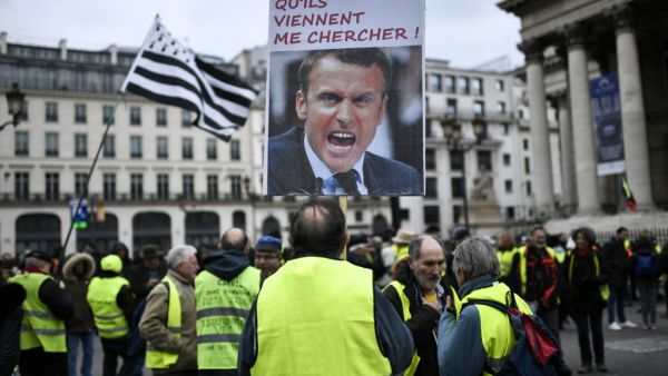 A protester holds a sign depicting French President and reading "Let them come and get me !" on the Place de la Bourse in Paris during a demonstration called by the "Gilets Jaunes" (Yellow Vests) movement on December 28, 2019, as part of a nationwide multi-sector strike against French government's pensions overhaul. STEPHANE DE SAKUTIN / AFP