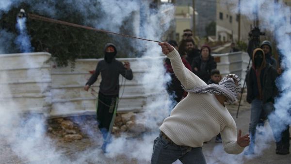A Palestinian demonstrator uses a slingshot to return a tear gas canister toward Israeli forces during clashes with them following a weekly protest against the expropriation of Palestinian land by Israel, in the village of Kfar Qaddum, in the occupied West Bank on January 10, 2020. JAAFAR ASHTIYEH / AFP