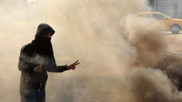 A masked anti-government protester gestures the victory sign as he runs from tear gas fired by security forces during clashes in the central Iraqi holy shrine city of Karbala on January 20, 2020. Mohammed SAWAF / AFP