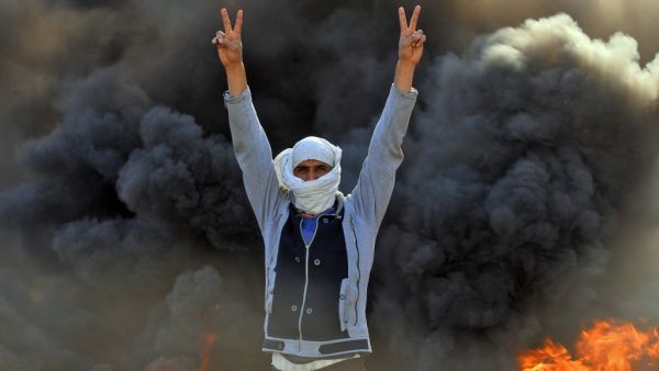 A masked anti-government protester flashes the victory gesture as he stands before flaming tyres at a make-shift roadblock in the central Iraqi holy shrine city of Najaf on January 27, 2020. Haidar HAMDANI / AFP