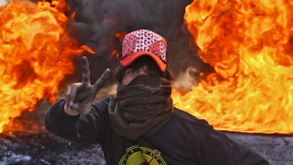 A masked anti-government protester flashes the victory gesture as he stands before flaming tyres at a make-shift roadblock in the central Iraqi holy shrine city of Najaf on January 27, 2020. Haidar HAMDANI / AFP