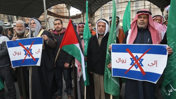 Palestinian protesters stand with Palestinian and Hamas (green) flags and hold up signs showing the Israeli flag defaced with a red X mark and with words in Arabic reading "to demise" during a demonstration against US President Donald Trump's Middle East peace proposal in Khan Yunis in the southern Gaza Strip on February 3, 2020. SAID KHATIB / AFP
