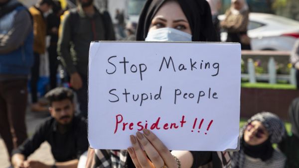 An Iraqi anti-government protester wearing a protective mask lifts a placard during a student demonstration in the southern city of Basra, on February 6, 2020, after a night of violence blamed on supporters of a powerful cleric. AFP