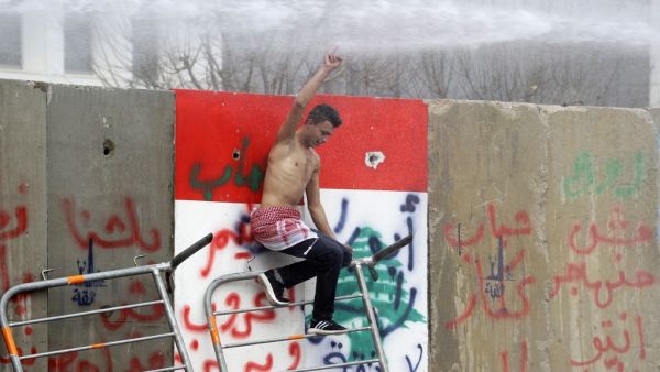 An anti-government protester climbs cement blocks protecting state institutions in central Beirut during protests on February 11, 2020 to stop a confidence vote for a new government, which they say fails to address their demands and cannot rescue the ailing country. Security forces used tear gas and water cannon to break up groups of demonstrators who hurled rocks at them and over the blast walls erected around parliament. Some lawmakers spent the night in parliament to thwart protesters who have successful