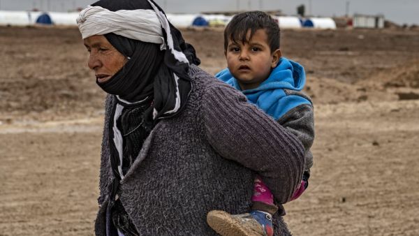 A Syrian woman walks by carrying a child on her back in the Washukanni Camp for the internally displaced, near the predominantly Kurdish city of Hasakeh in northeastern Syria, on February 17, 2020. Delil SOULEIMAN / AFP