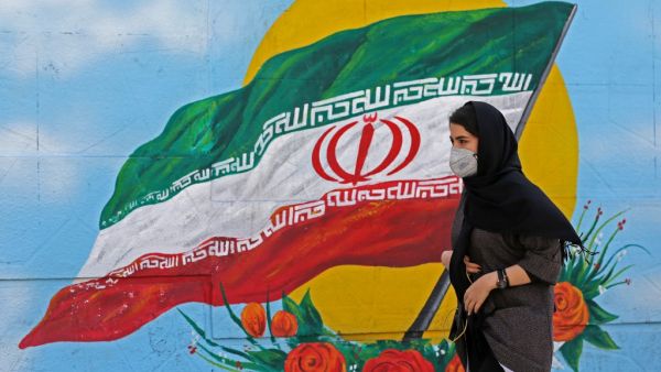 Iranians wearing masks walk past a mural displaying their national flag in Tehran on March 4, 2020. Iran has scrambled to halt the rapid spread of the COVID-19 virus, shutting schools and universities, suspending major cultural and sporting events, and cutting back on work hours.  ATTA KENARE / AFP