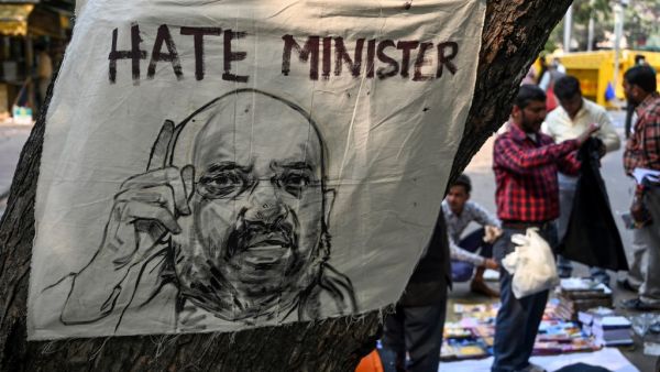 A street vendor selling clothes stands behind a poster displaying a drawing of Home Minister Amit Shah (L) during a protest against India's new citizenship law in New Delhi on March 4, 2020. Sajjad HUSSAIN / AFP