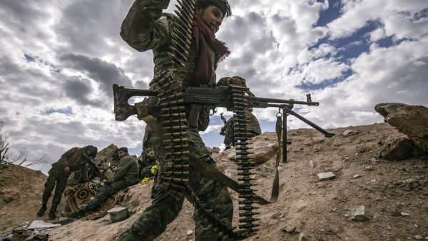 In this file photo taken on March 17, 2019, a fighter of the Syrian Democratic Forces (SDF) walks carrying a machine gun at a position close to the camp of Baghouz where remaining Islamic State (IS) group fighters and their families are holding out in the last position controlled by IS, awaiting to advance on them in the countryside of the eastern Syrian province of Deir Ezzor. As it enters its tenth year, the war in Syria is anything but abating as foreign powers scrap over a ravaged country where human su
