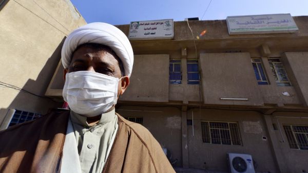 A cleric wearing a protective mask stands outside the building of a religious school which attracts predominantly foreign students and where the first Iraqi case of novel coronavirus infection was confirmed, during its disinfection in the central Iraqi shrine city of Najaf, on March 9, 2020. Haidar HAMDANI / AFP