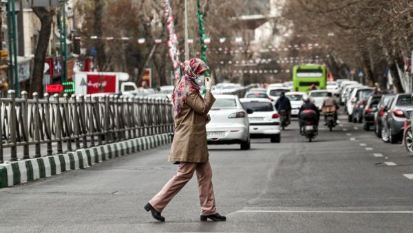 A woman wearing a protective face mask and latex gloves crosses a street in Iran's capital Tehran on March 14, 2020. STRINGER / AFP