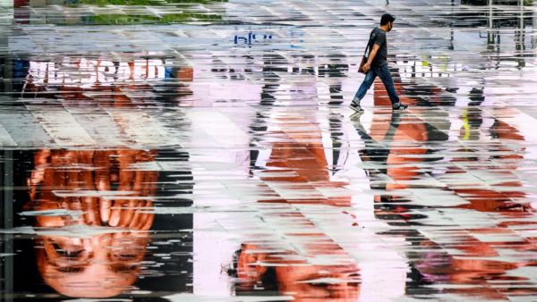 A man wearing a facemask, amid concerns over the spread of the COVID-19 coronavirus, walks among puddles reflecting advertisement screens on an empty square in Bangkok on March 15, 2020. Mladen ANTONOV / AFP