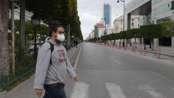 A man wearing a face mask crosses a street at Habib Bourguiba Avenue in Tunis on March 18, 2020 shortly before a night curfew imposed to halt the spread of coronavirus. Tunisia has reported 24 coronavirus cases and while no deaths have been reported in the country, the virus has killed more than 6,000 worldwide. FETHI BELAID / AFP