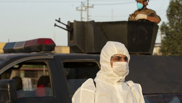 A member of the Iraqi security forces stands guard atop a military vehicle as a health worker wearing a protective outfit walks by during a curfew imposed as a measure to stem the spread of the novel coronavirus in the southern city of Basra on March 19, 2020. The US-led coalition is temporarily withdrawing training forces from Iraq as a protective measure against the novel coronavirus, a senior official in the alliance said today. Iraqi health officials have confirmed 13 deaths and more than 170 cases of C