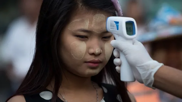A woman wearing thanaka, a traditional facial cosmetic, has her temperature taken as a preventive measure against the COVID-19 novel coronavirus at a market in Yangon on March 21, 2020. Ye Aung Thu / afp