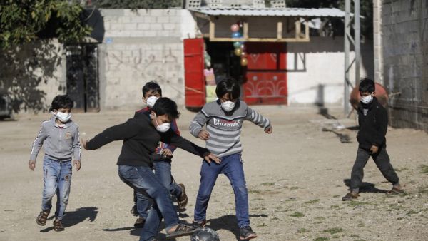 Boys wearing protective and N95 masks play with a football outside their homes in Gaza City on March 22, 2020. MOHAMMED ABED / AFP