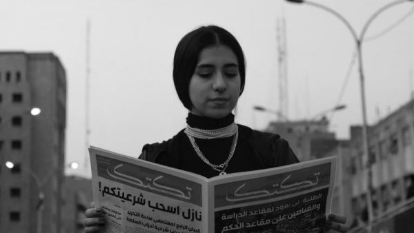 A hunt for the right moment. A young woman reads a newspaper near Tahrir Square in Baghdad during protests. (Amir Hazim)