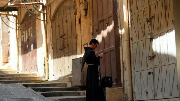 A Fransiscan friar checks his mobile phone in front of closed shops, in the Old City of Jerusalem on March 16, 2020, after Israel imposed tight restrictions to contain the COVID-19 coronavirus disease. In the millenary alleys of Jerusalem's Old City where a crowd of visitors usually walks the alleys, the sellers of ceramics, T-shirts and rugs have no one left to woo. Emmanuel DUNAND / AFP