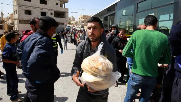 People queue to buy subsidised bread from a municipal bus in the Marka suburb in the east of Jordan's capital Amman on March 24, 2020, as the kingdom announced it would deliver bread and water supplies after the government decided to indefinitely extend a curfew amidst efforts to contain COVID-19 coronavirus disease. Jordan imposed a curfew after citizens failed to heed instructions not to leave home except for emergencies, and it has deployed the army to enforce the measure. A fleet of 190 buses chartered 